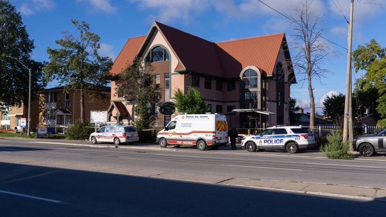 A van with fire department markings and police car out front of a building that's blocked by yellow tape.