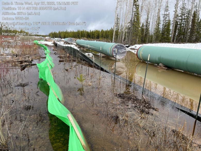 A fence is visible beneath puddles of water, near some tall pipes.