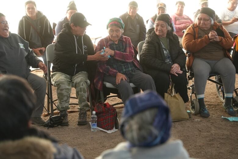 Innu elders sit on chairs in a circle, playing a game of pass the package.