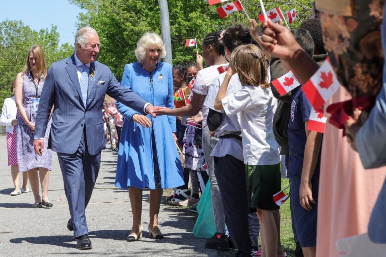 Two people greet schoolchildren who are holding Canadian flags.