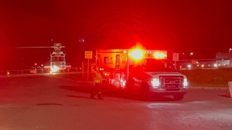 An ambulance with flashing lights is pictured at night with a helicopter in the background.