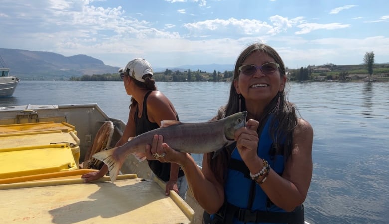 A woman with sunglasses on poses with a fish she caught on a boat.