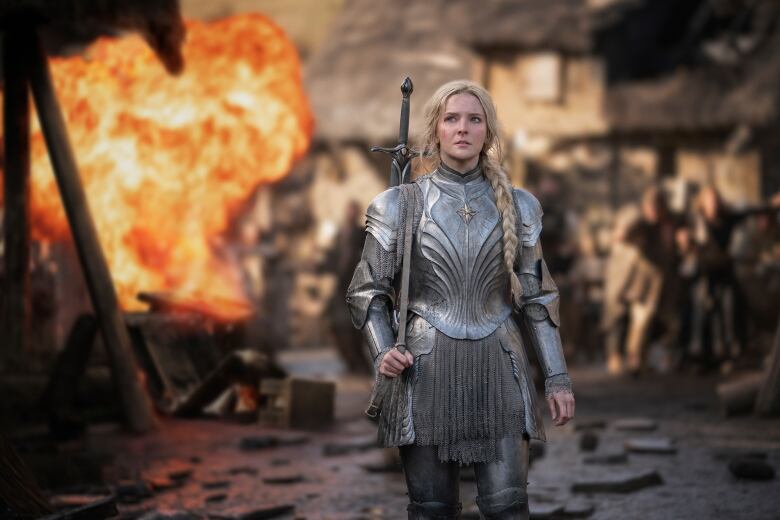 An actress wearing armour is shown standing in front of an explosion in a scene from a TV show.