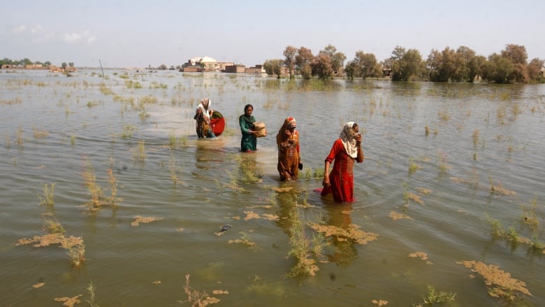 Four women, in a line, wade through flood waters. 