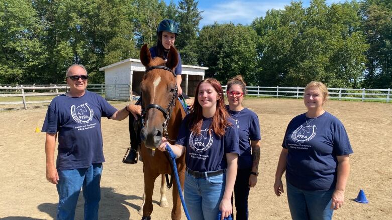 A group of people stand around a girl on a horse. 