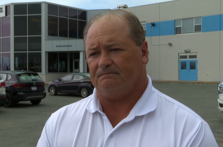 A man in a white shirt stands in front of a glass union building.