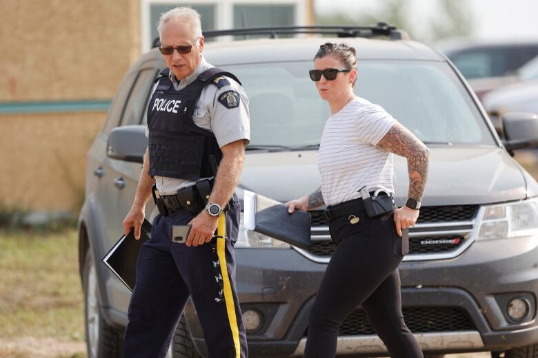 A uniformed RCMP officer and a plain clothes investigator walk past a vehicle in the aftermath of a stabbing spree on James Smith Cree Nation in September 2022.