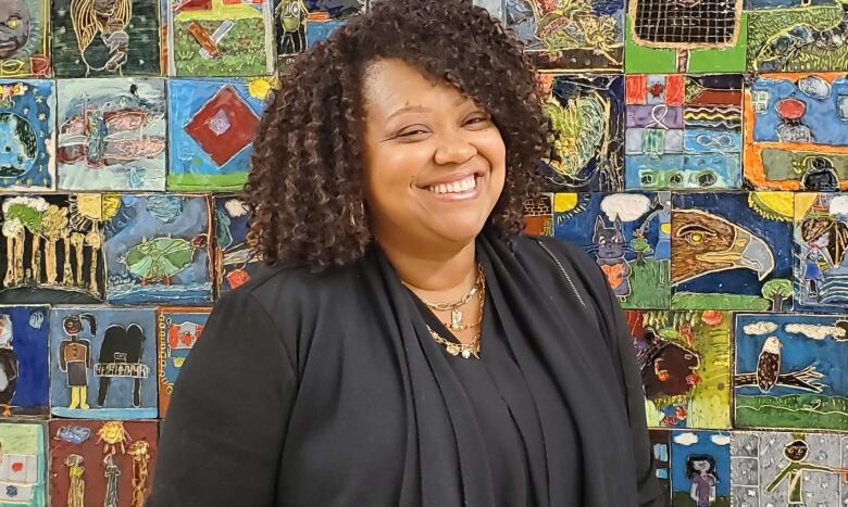 A woman stands in front of a wall of children's painting and smiles at the camera.