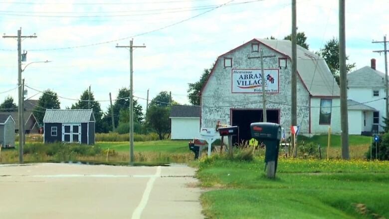 A rural scene includes a barn with a large sign saying in French and English 'Welcome to Abram-Village.'