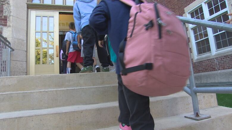 Students wearing backpacks walk up the stairs into a school.