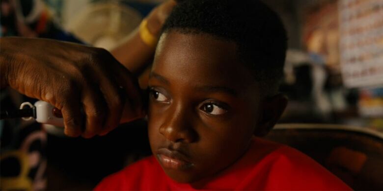 A small boy looks off camera as he receives a haircut. 