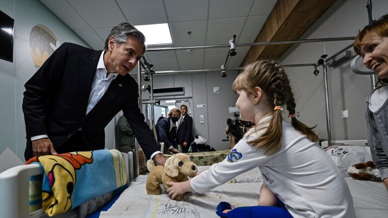 A man hands a stuffed animal to a child on a hospital bed.