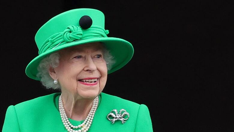 A woman in a green hat and dress looks upwards.