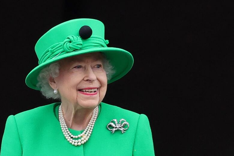 A woman in a green hat and dress looks upwards.