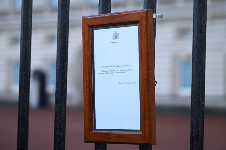 A framed notice hangs on a black metal fence. 