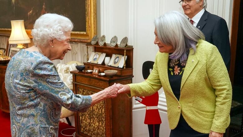 Two people shake hands as another person looks on.