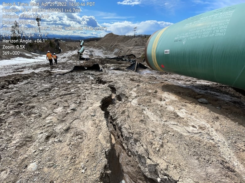 Cracks are seen in dry soil with a green pipe to the right of it.