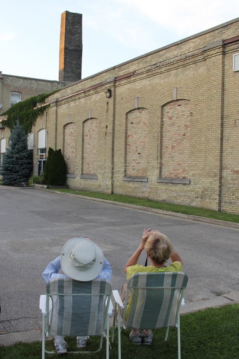 Two women sit in lawn chairs looking at an old chimney with binoculars 