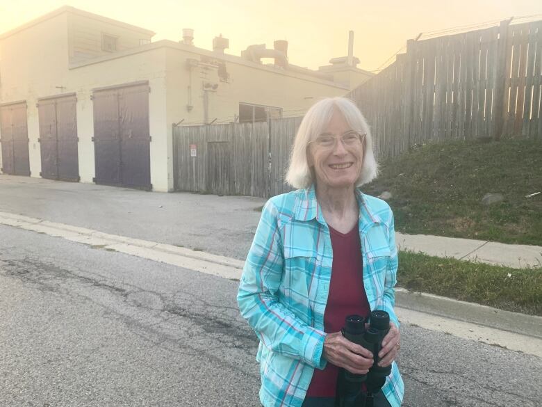 woman stands outside an old factory holding binoculars