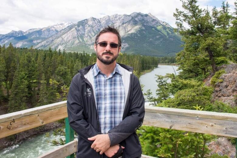 A man stands with mountains in the background.