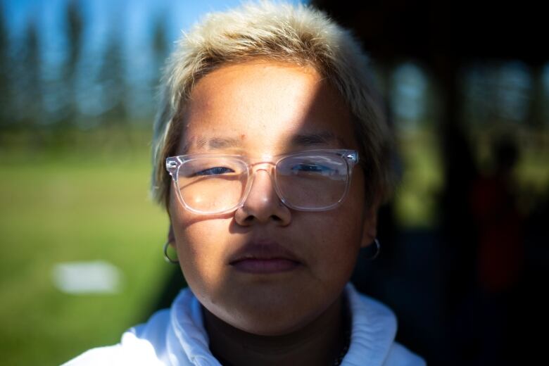 A young person with short hair has their face half covered and shadow and half covered in light.