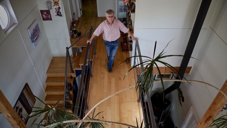 Ross MacLeod holds two handrails atop a flight of stairs in a narrow corridor in his home.