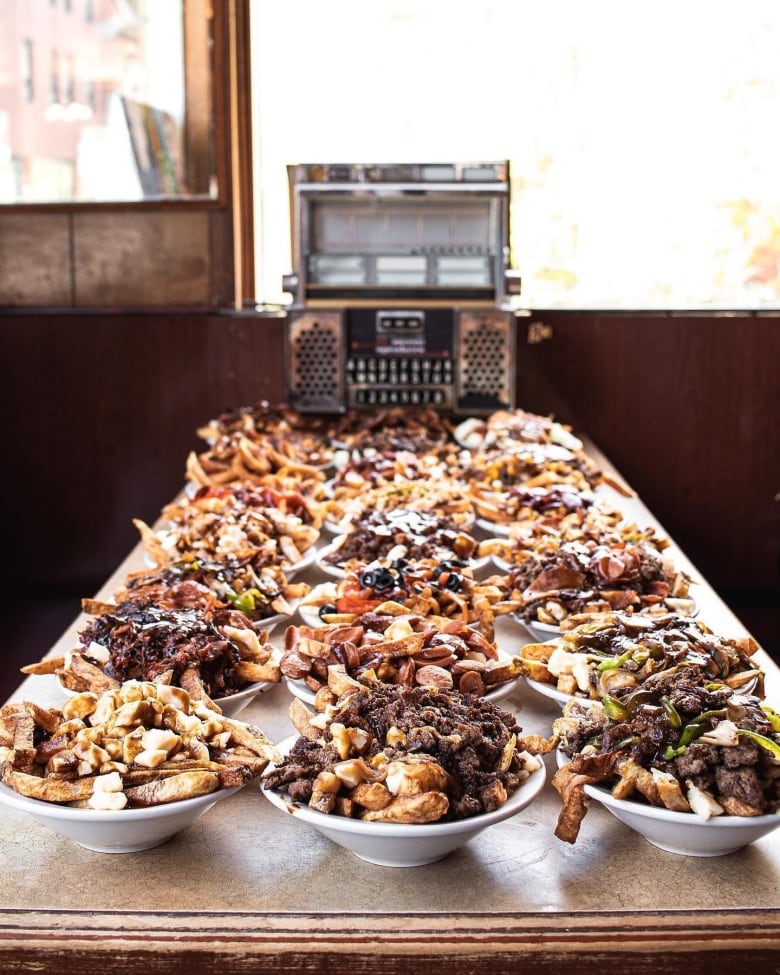 A diner table overflows with bowls of poutine. 