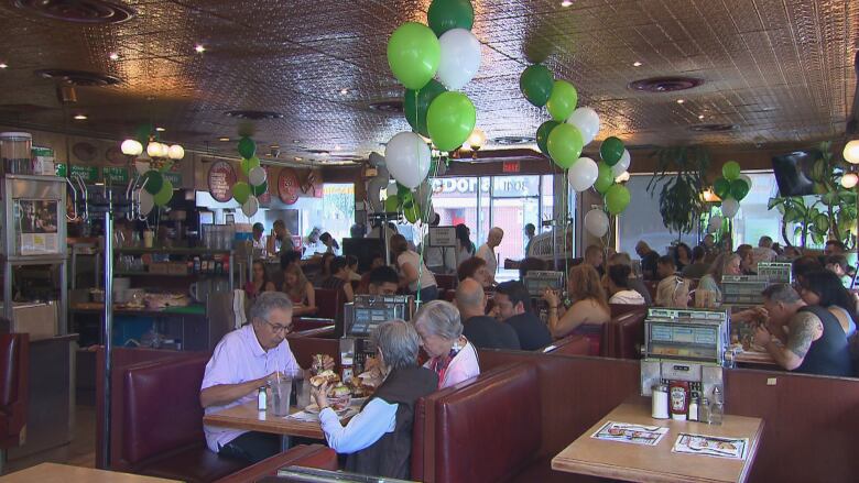 A crowded diner decorated with green and white balloons.