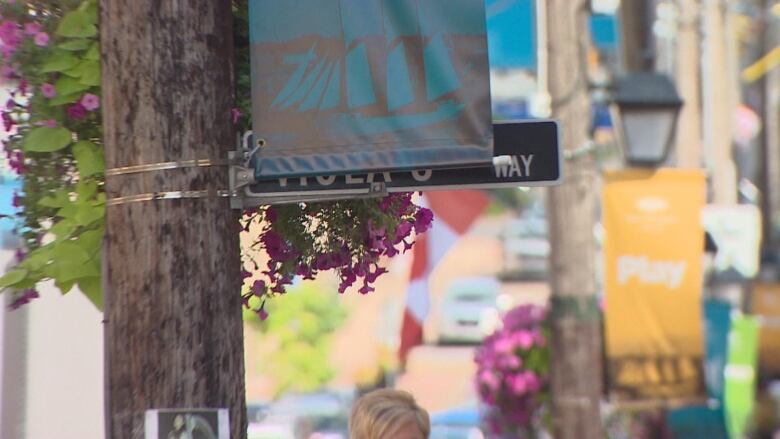 A street sign hidden by a banner and a plant basket