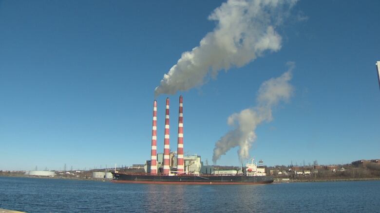 Three red and white hooped chimneys are shown on the shore with a ship in front of them.