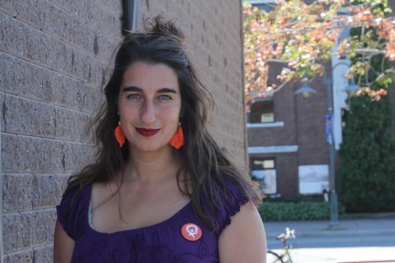 A portrait of a woman wearing a purple top and an orange campaign button.