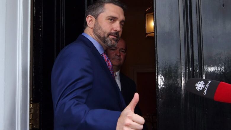 Man in suit gives thumbs up in doorway.