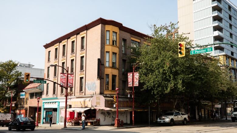 The intersection of Gore and Pender streets in Vancouver's Chinatown is shown, including a four-storey yellow building with a market open on the corner.