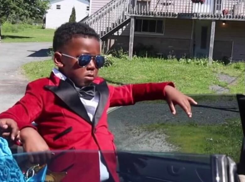 Image of a young boy wearing a red blazer with a black satin lapel and dark aviator glasses.