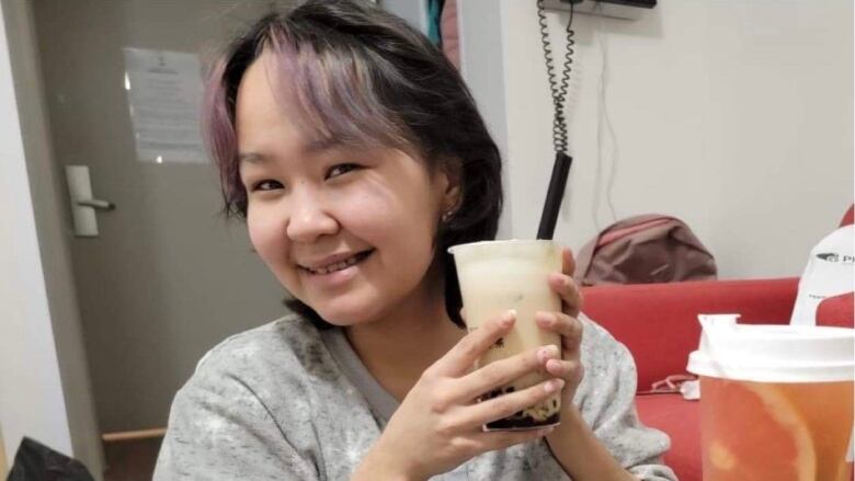 Woman holds bubble tea drink up, smiling. 