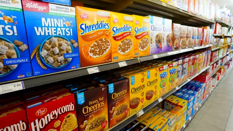 A grocery store shelf with several differents brands of cereal. 