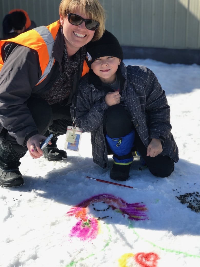 A woman and a boy smile while showing off a painting in the snow.