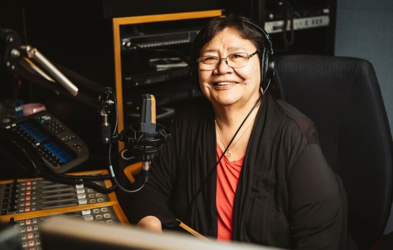 A woman with a black sweater sitting at a radio desk.