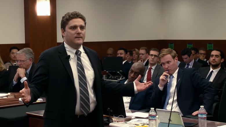 Brent Wisner, a white man in his 30s, presents to a jury out of frame. Spectators and other members of the legal team are visible in the background.