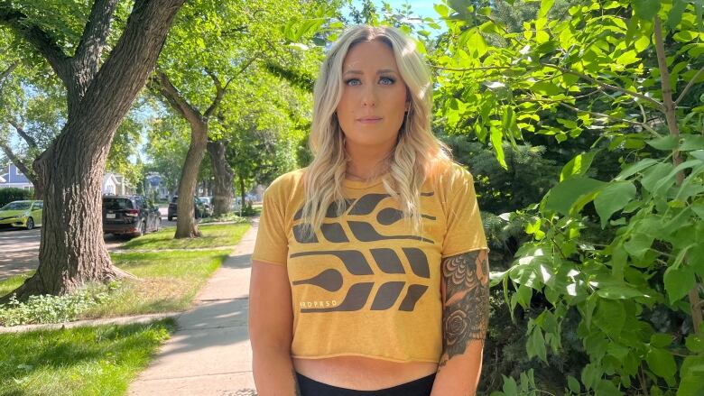 A woman stands on a sidewalk lines by green foliage and trees.