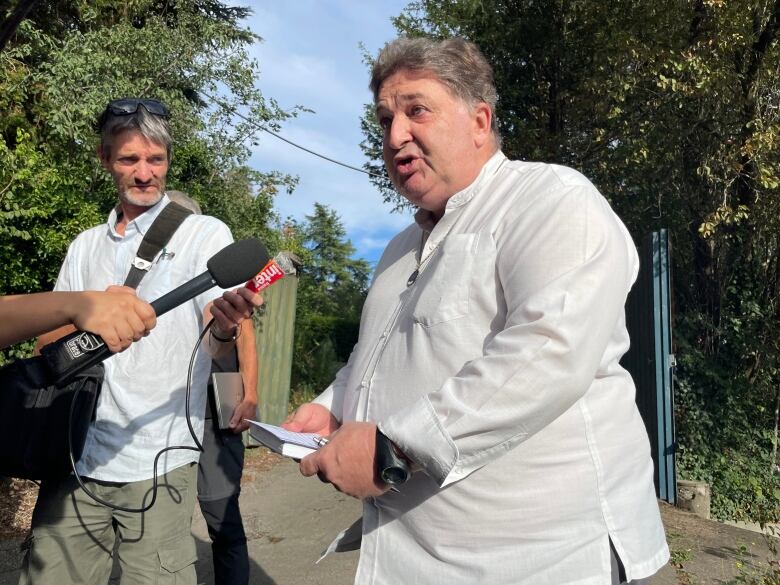 A man speaks into a microphone on a street.