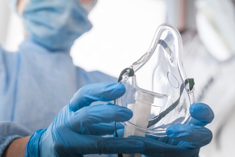 A respiratory therapist with blue-gloved hands holds out an oxygen mask.