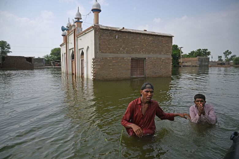 Two desperate men wade through water in a flood.