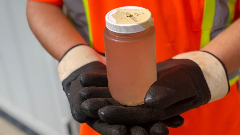 Two hands hold up a jar with brown liquid in it.