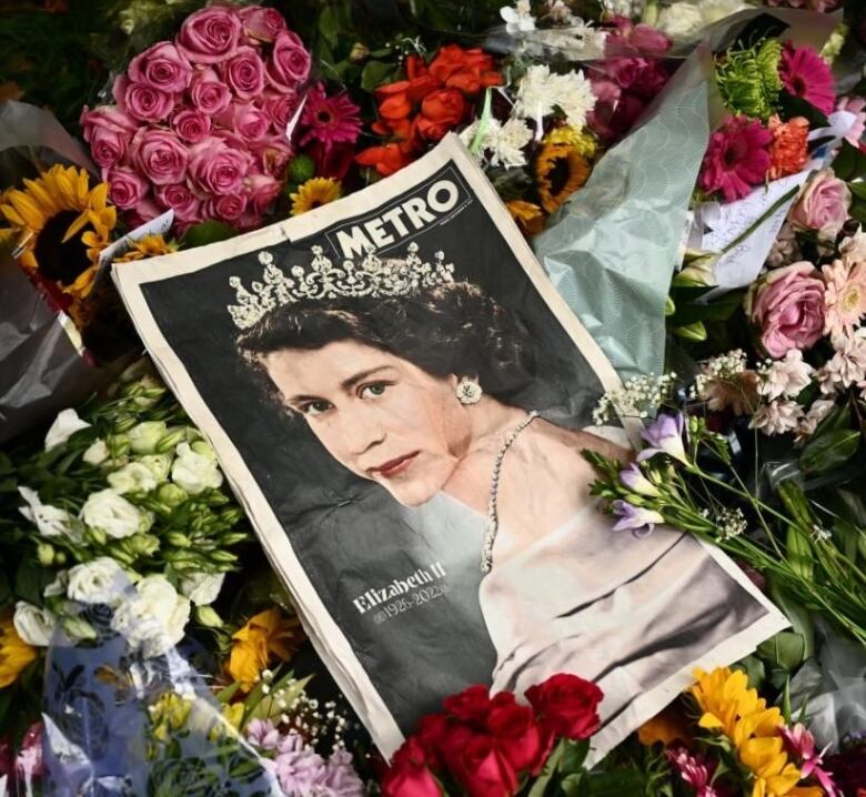 A newspaper with a young Queen's image sits on top of a pile of flowers placed as a memorial. 