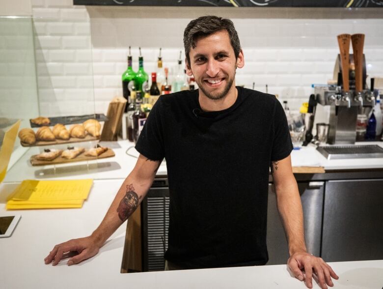 A man smiles from behind a coffee shop counter.