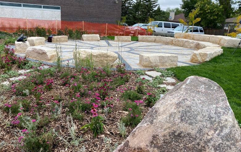 A paved circle surrounded by large stones for seating, set amid a garden.