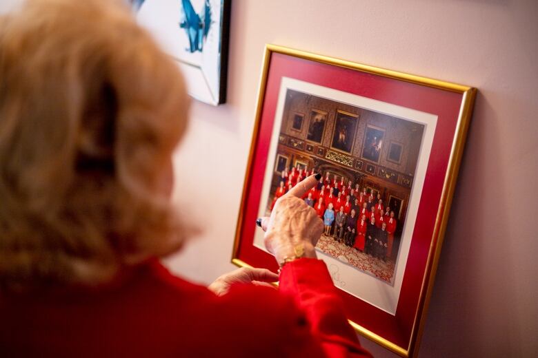 A woman points at a picture, depicting a group of caplains posing for a photo with the Queen of Englnad.