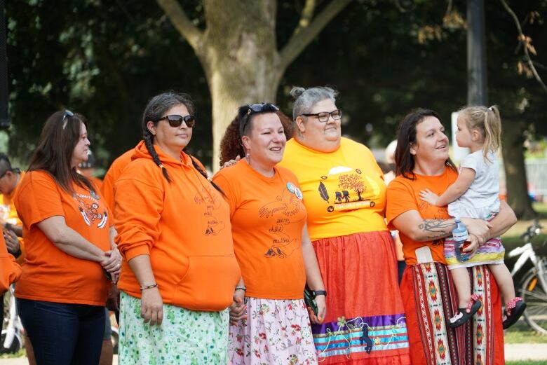 A group of women wearing orange shirts stand side by side holding hands.