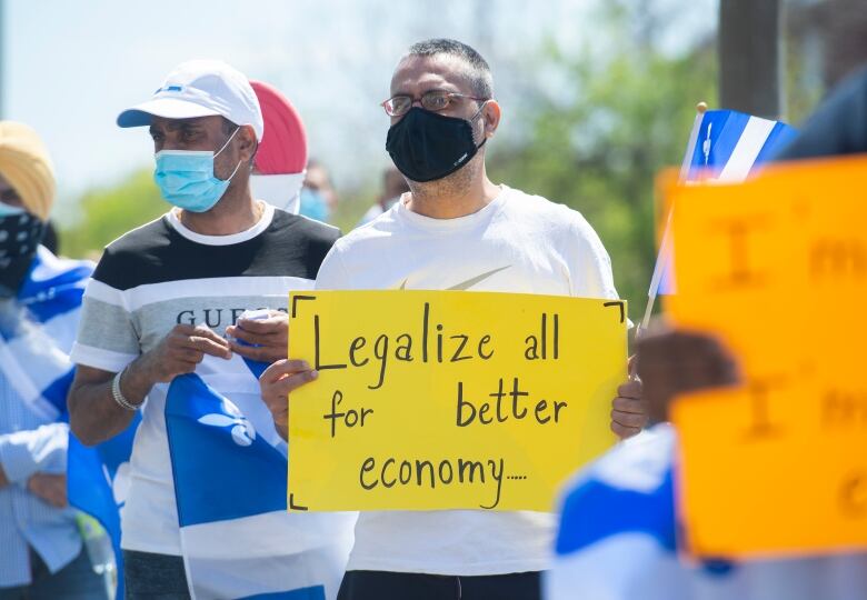 A man wearing glasses and a white T-shirt holds a yellow sign that reads: 